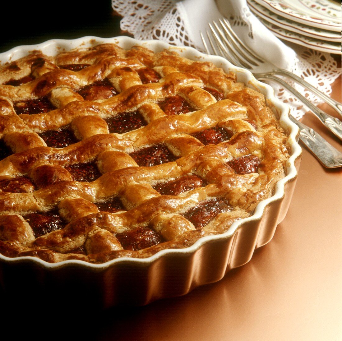 Linzer tart in baking tin; cake forks, plate, tablecloth