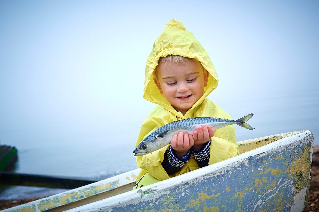 Boy wearing raincoat holding a mackerel