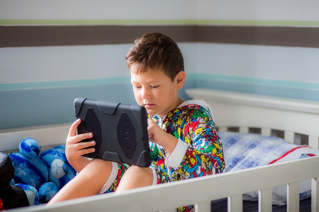 Boy sitting in bed using a digital tablet