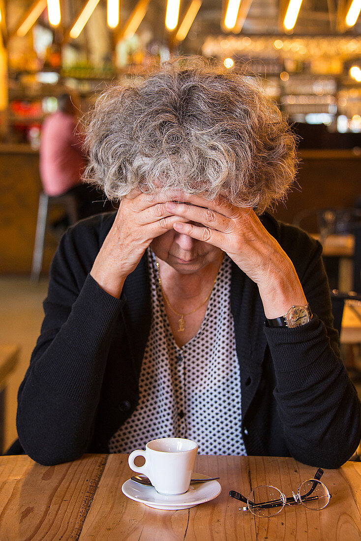 Senior woman in cafe with head in hands