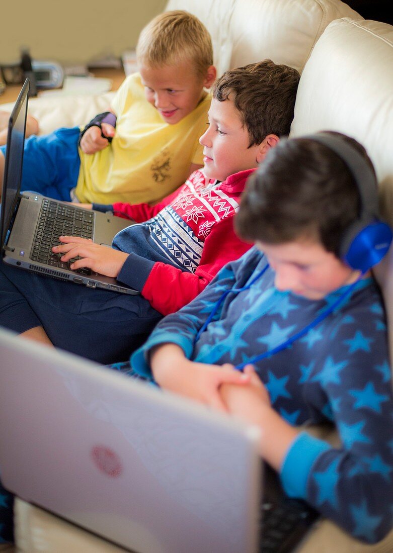Three boys using laptops sitting on sofa