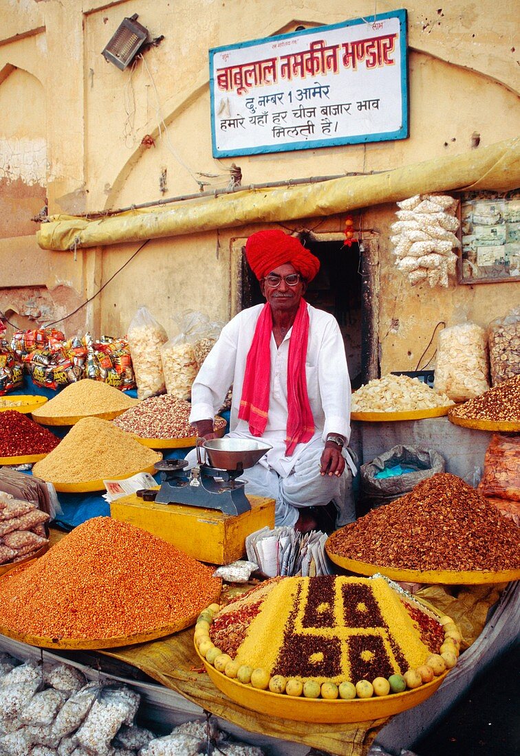 Indian spice seller sitting amongst spice baskets