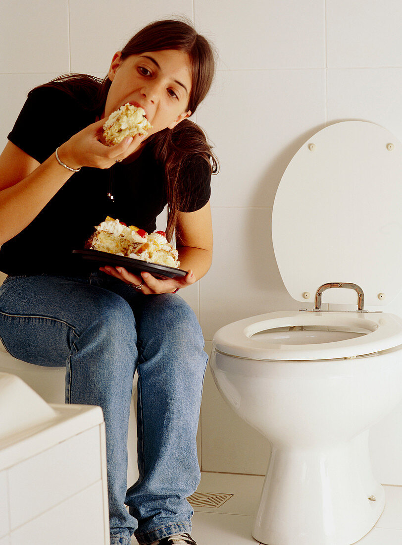 Bulimia: young woman eats alone at a toilet