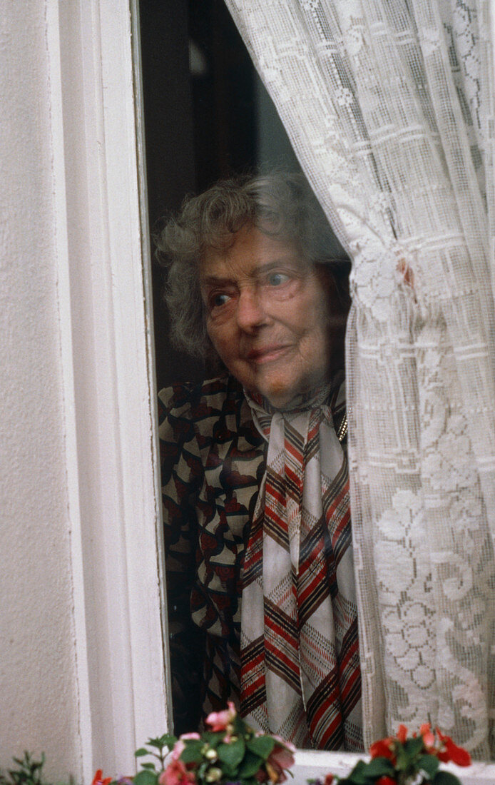 Elderly lady peering out of house window