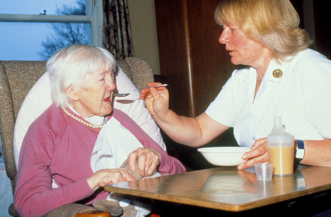 Nurse feeds elderly woman suffering from arthritis