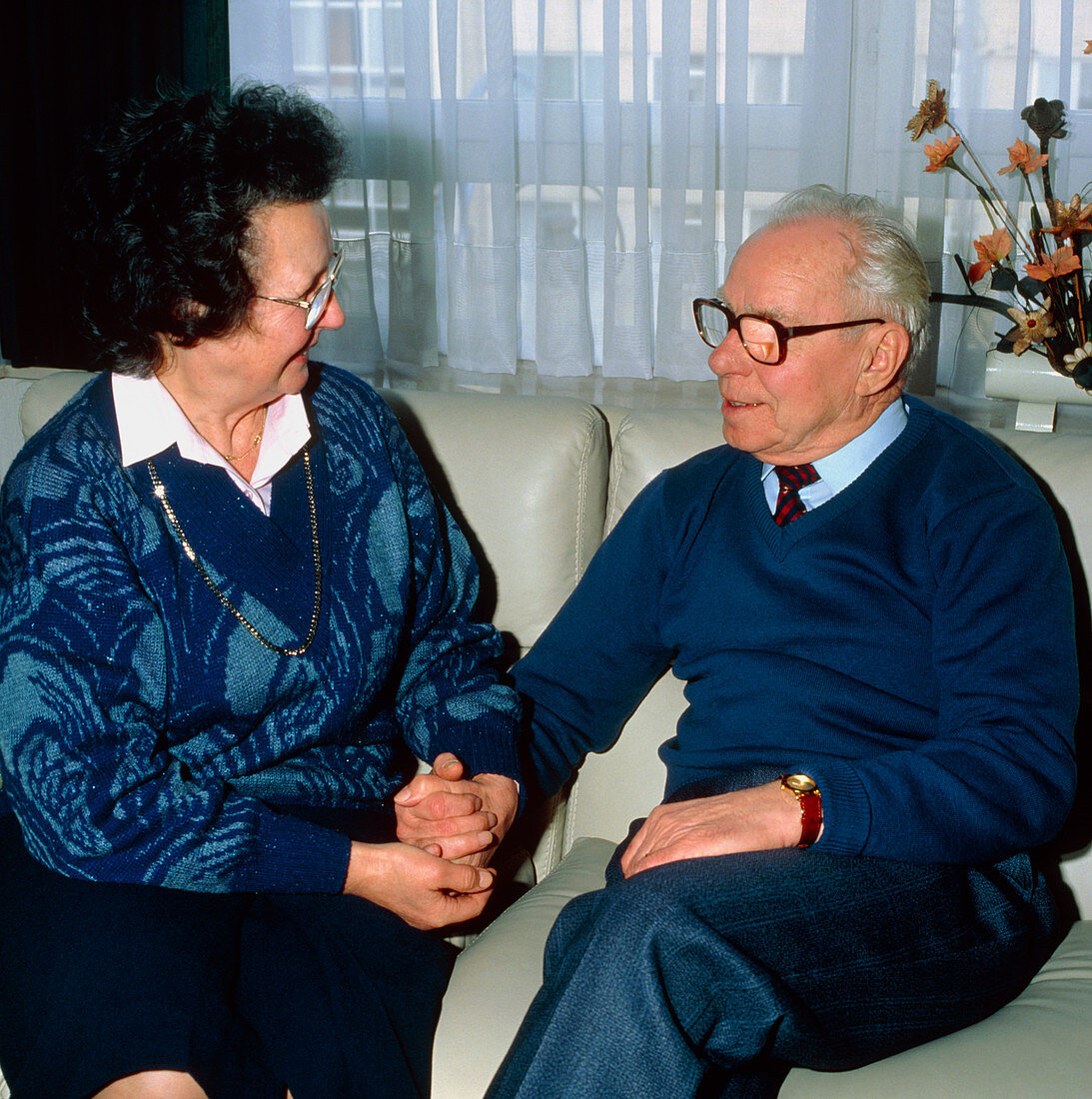 Elderly couple hold hands lovingly at home