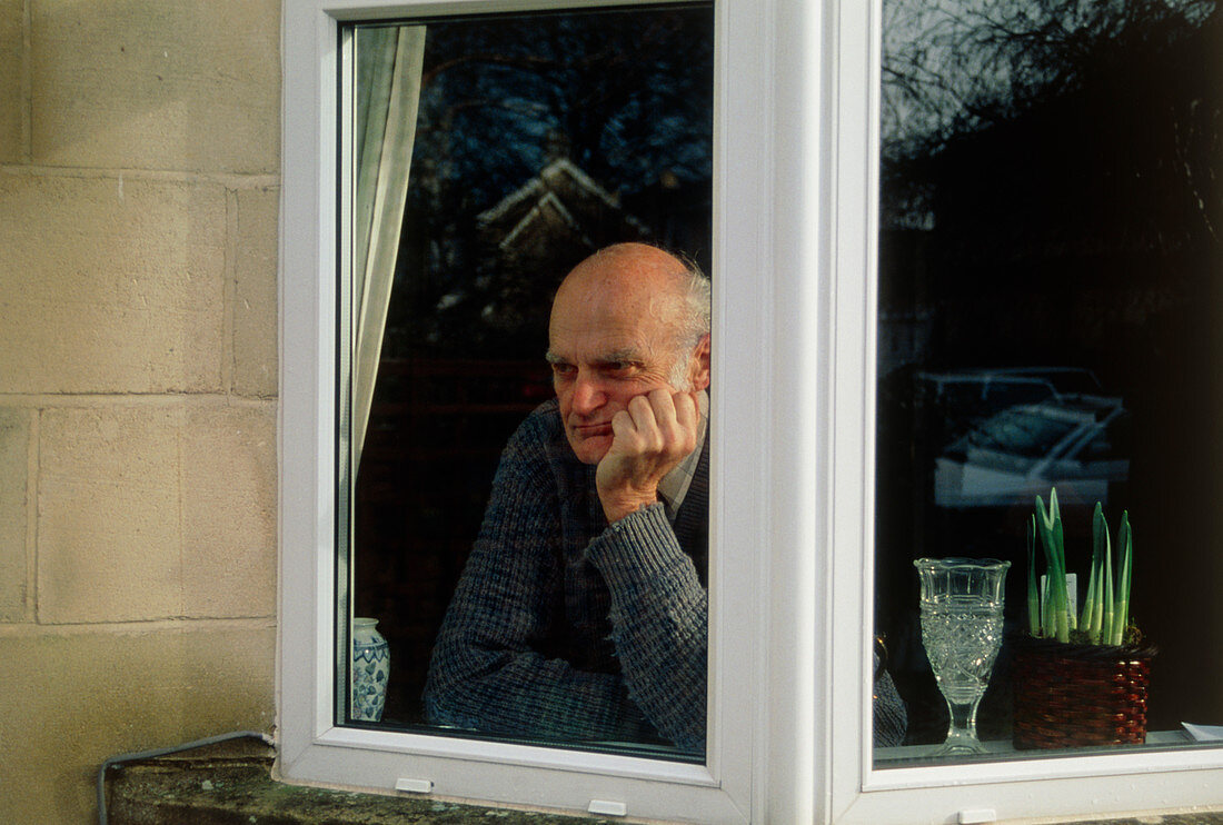 Depressed elderly man stares through a window