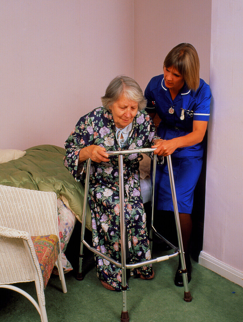 District nurse helps old woman use walking frame