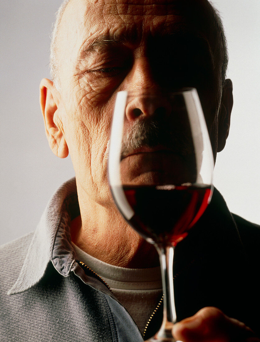 Elderly man examines a glass of red wine