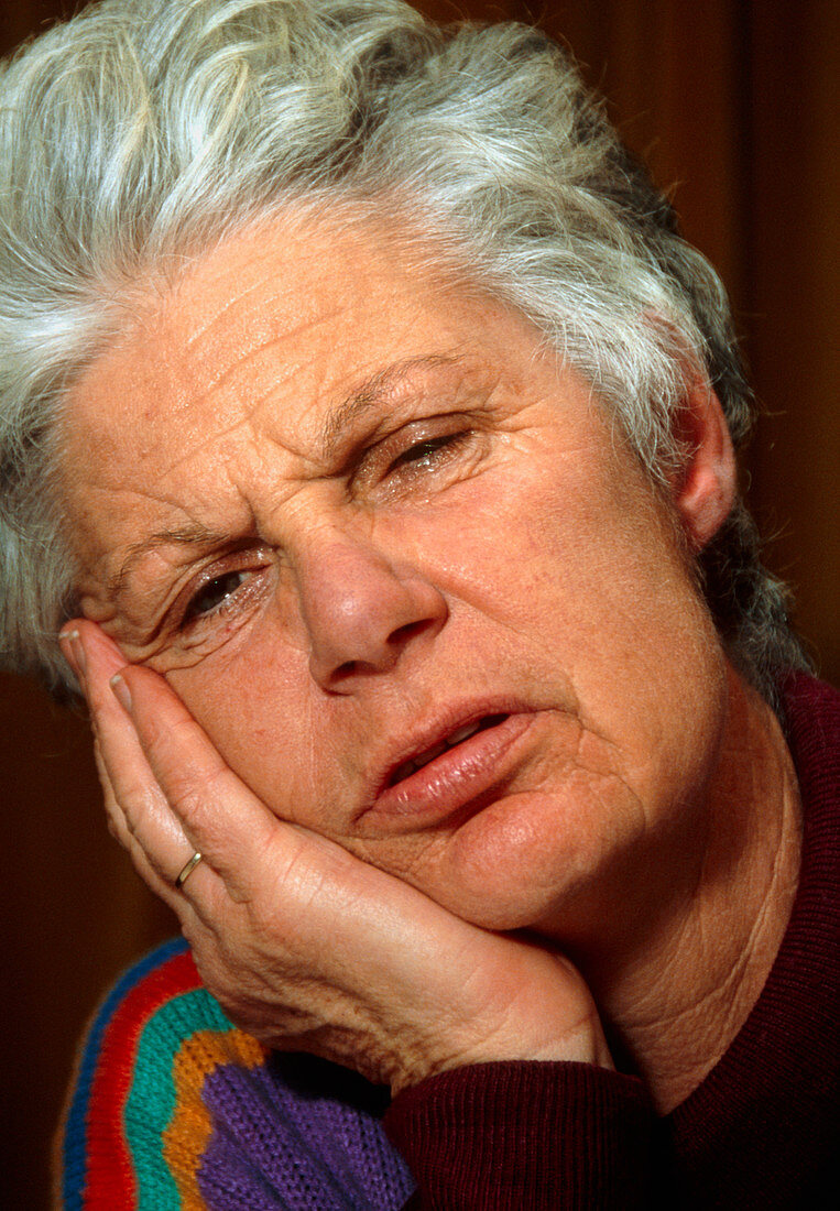 Elderly woman holds her jaw in expression of pain