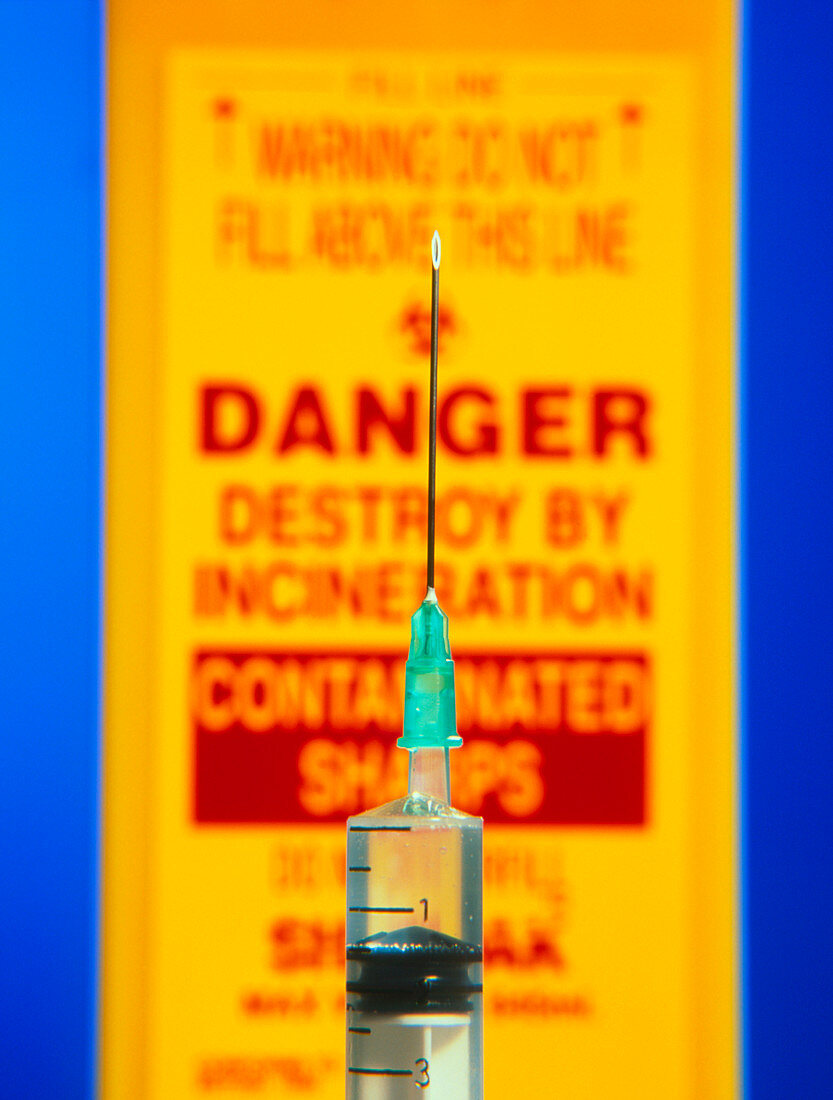 Close-up of syringe in front of sharps bin