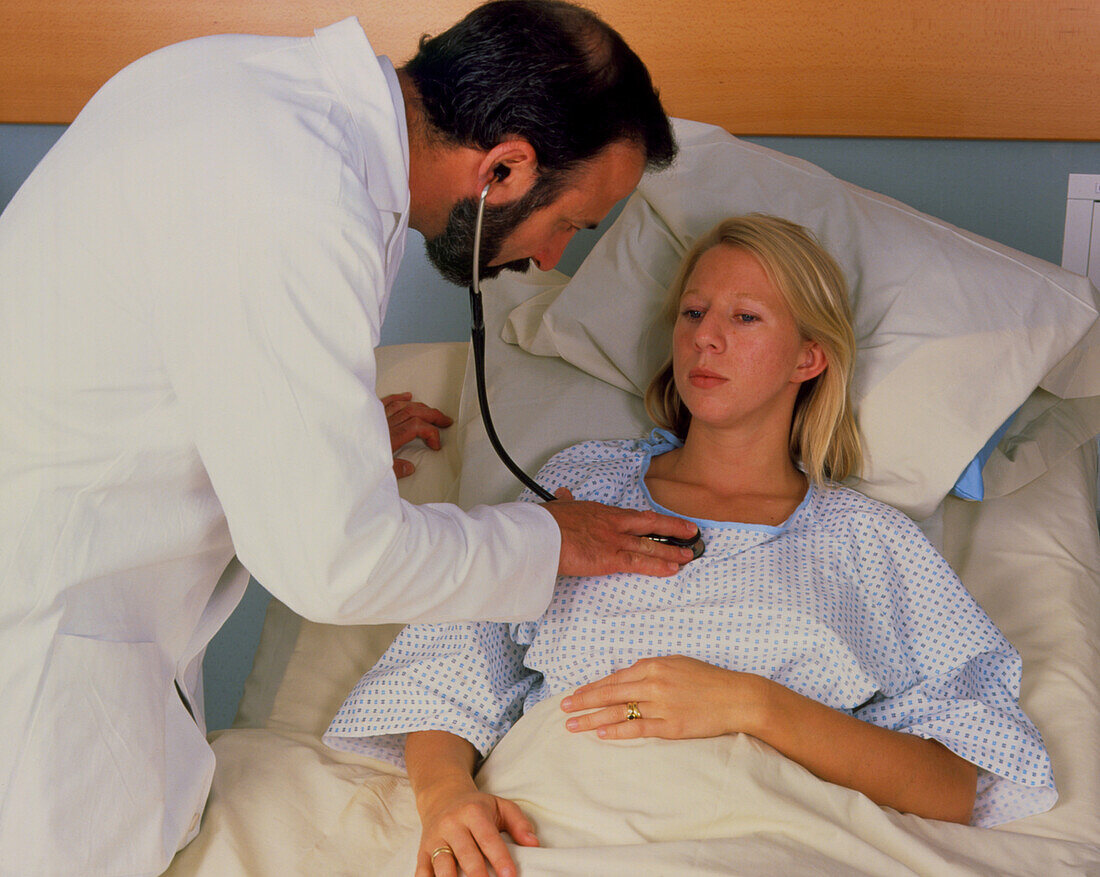 Doctor using stethoscope to examine woman in bed