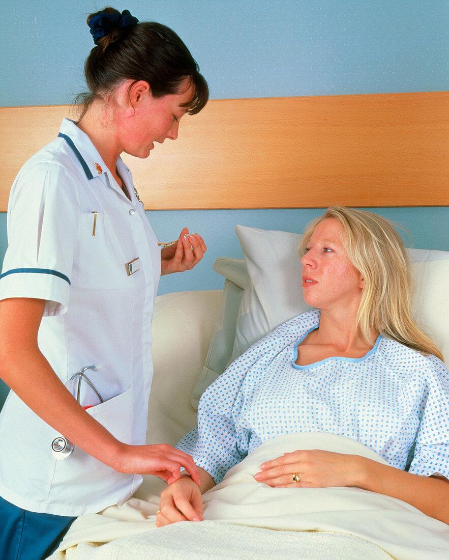 Nurse taking pulse of woman in hospital bed