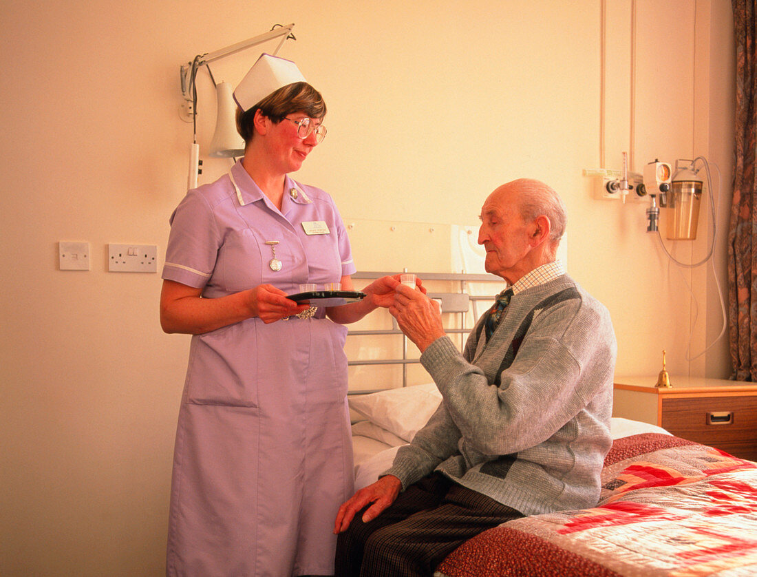 Nurse gives elderly man medication in a ward