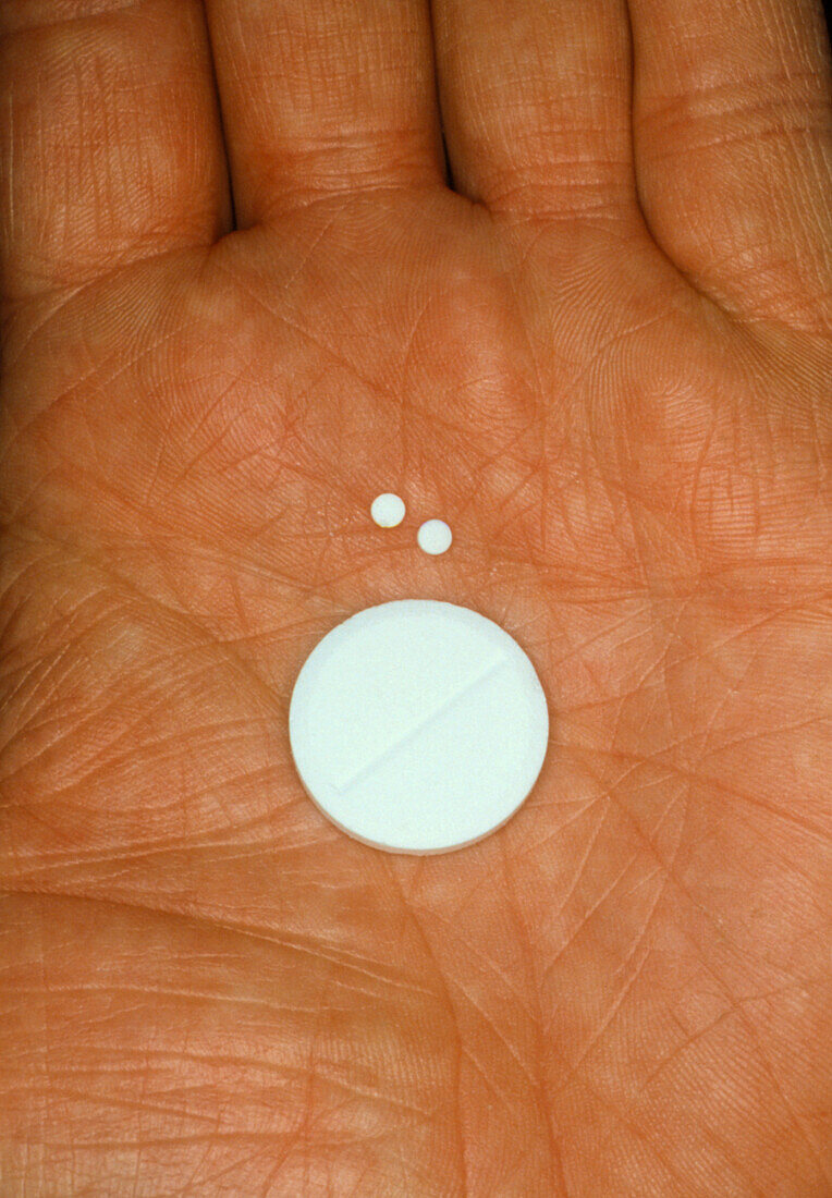 Hand holding pills of differing sizes