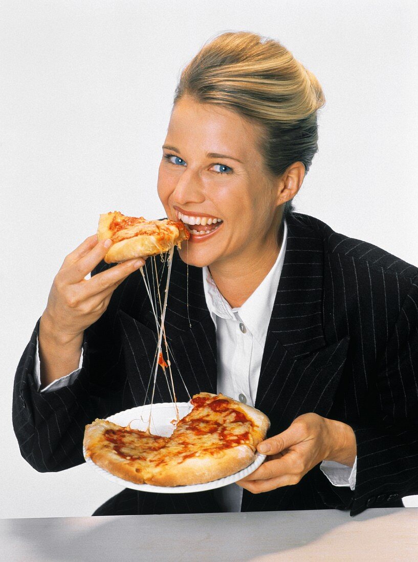 Junge blonde Frau in schwarzem Blazer isst eine Pizza
