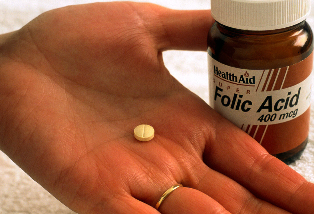 Pill of folic acid on woman's hand next to bottle