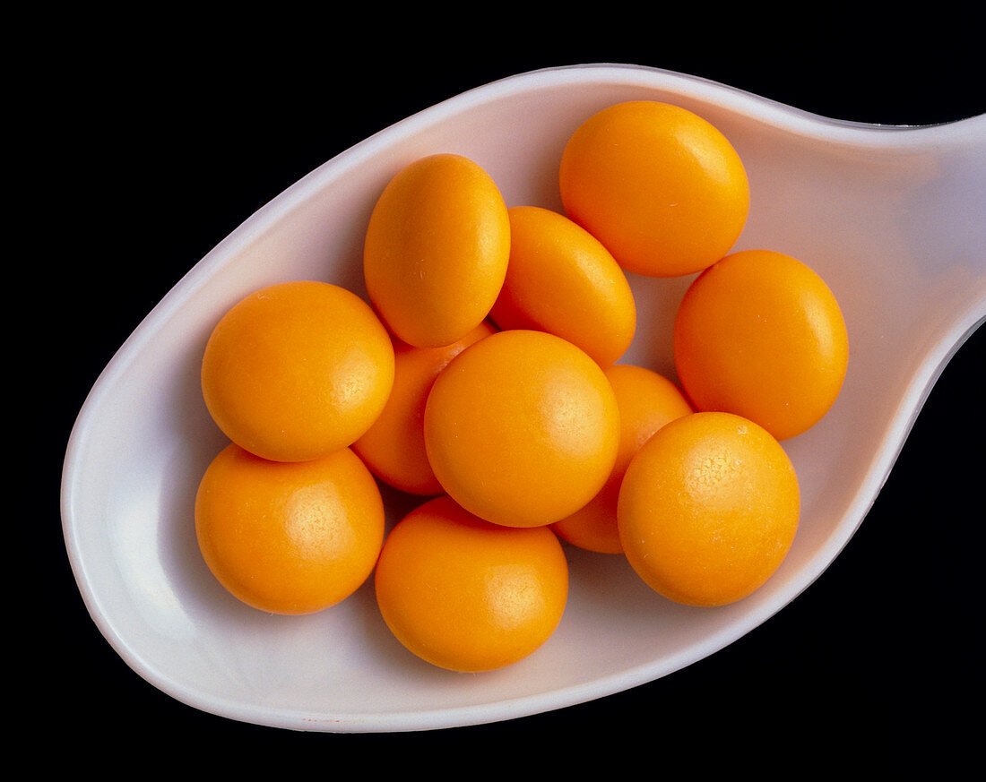 Orange multivitamins on a white plastic spoon