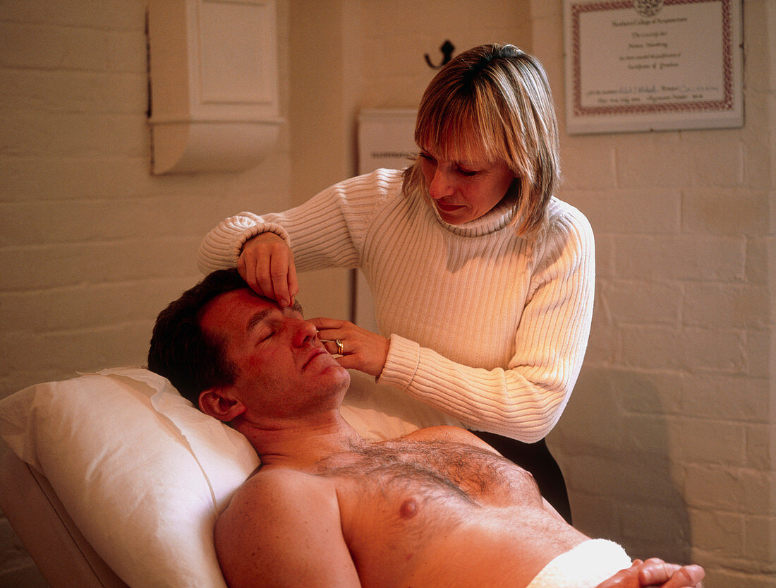 Woman inserting acupuncture needle into man's face
