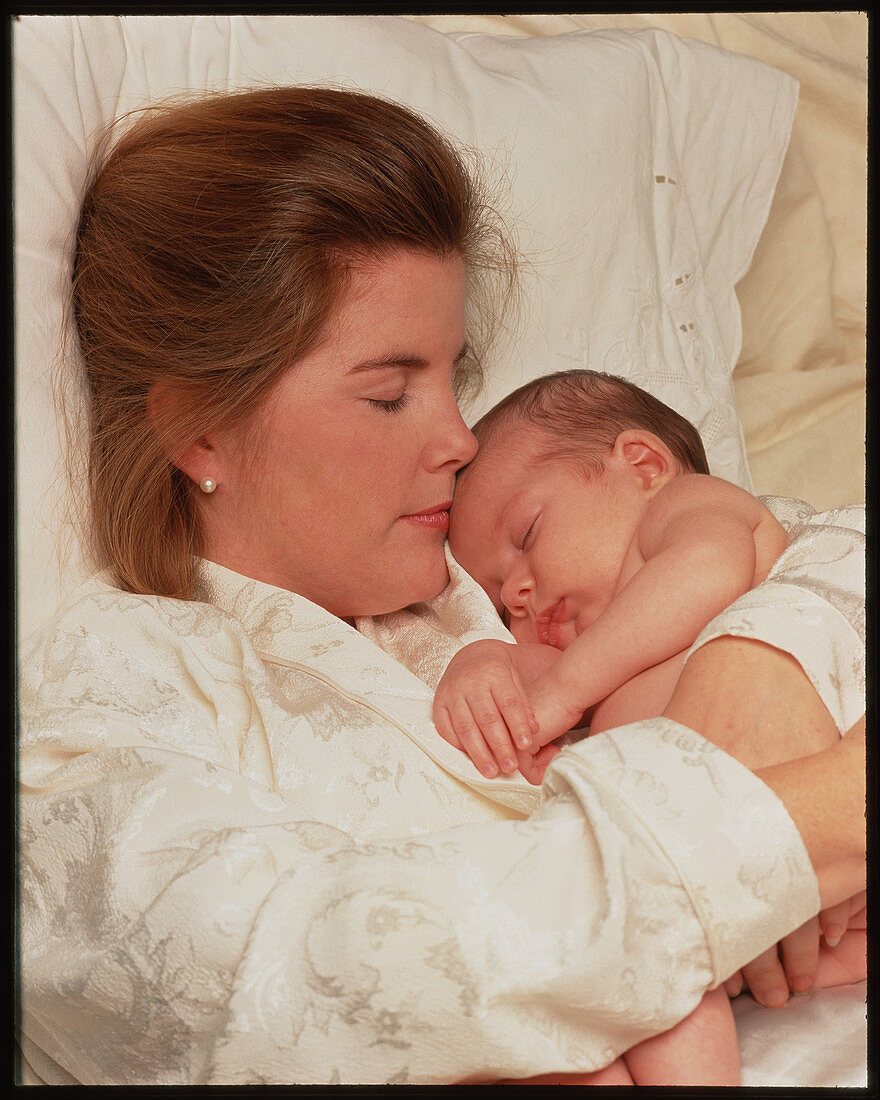 Healthy newborn baby cradled by its mother in bed