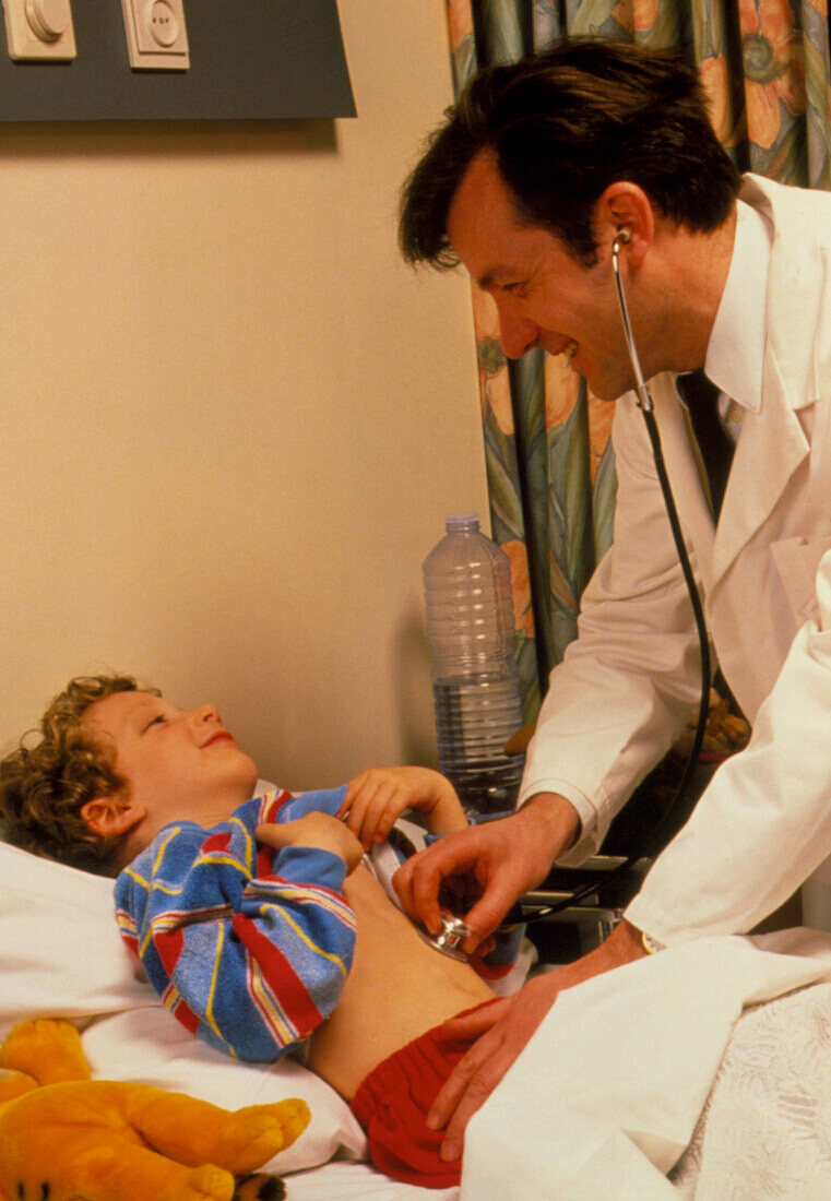 Doctor examining young boy in hospital bed