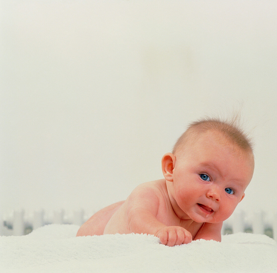 Naked 4-month-old baby girl crawling on towel