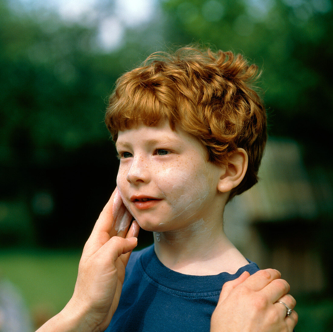 Mother's hands apply suncream to face of fair boy