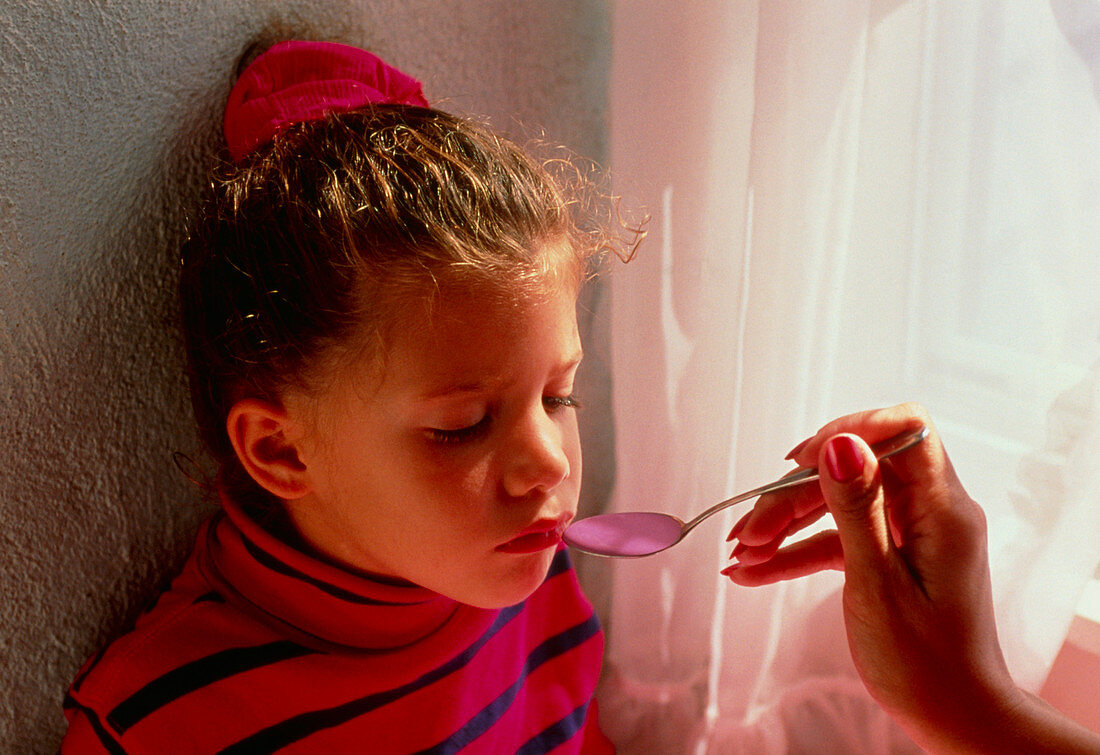 Sick young girl is fed a spoon of medicine