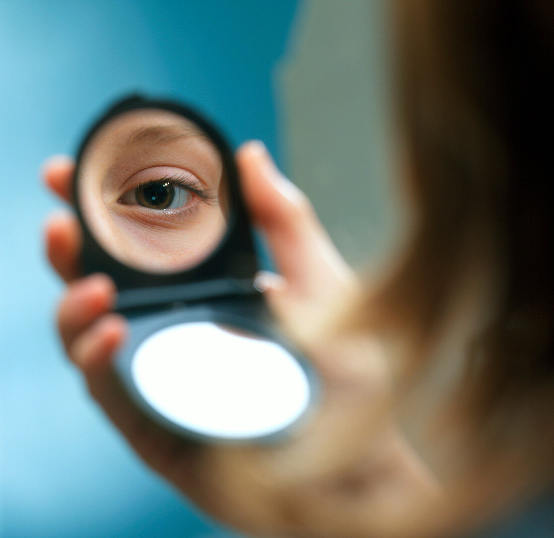 Woman examining her eye in a mirror