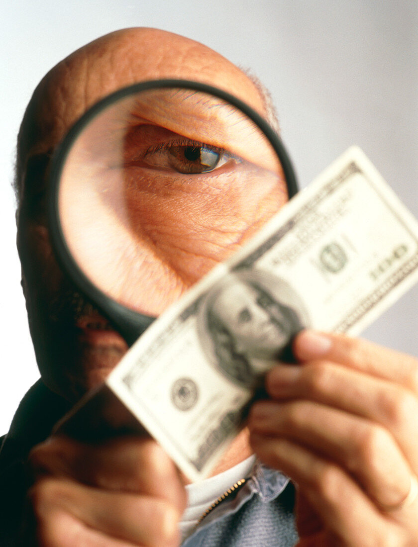 Man examines banknote with magnifying glass