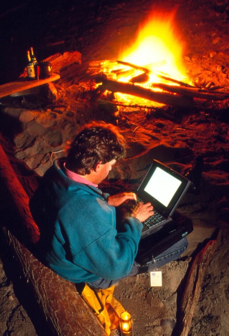 Man using a laptop computer by a campfire