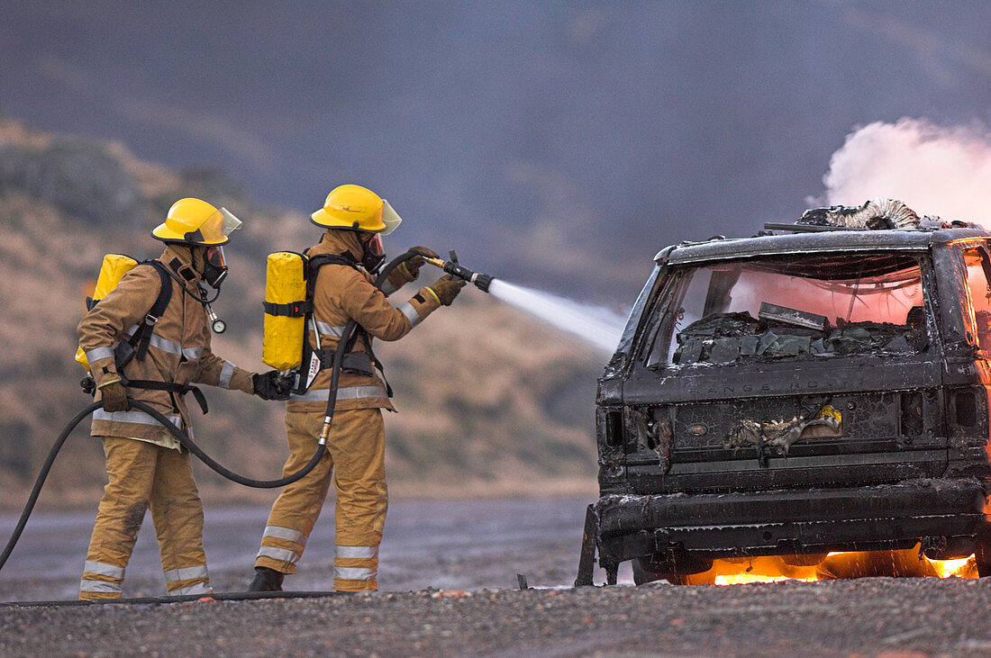 Firefighters hosing a burning car