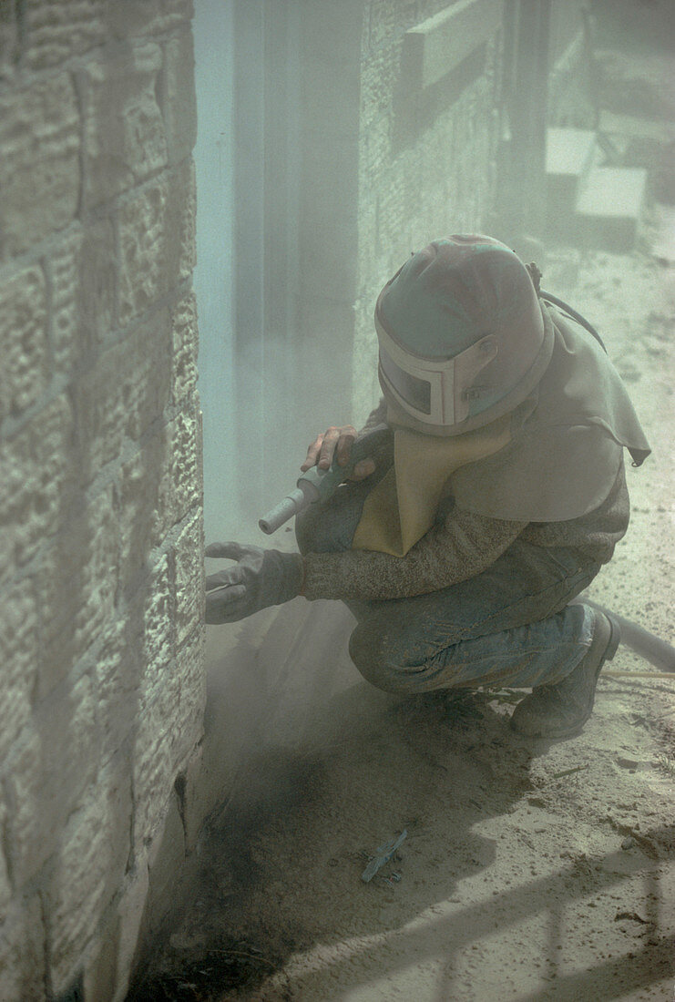 Man in protective clothing using sand blaster