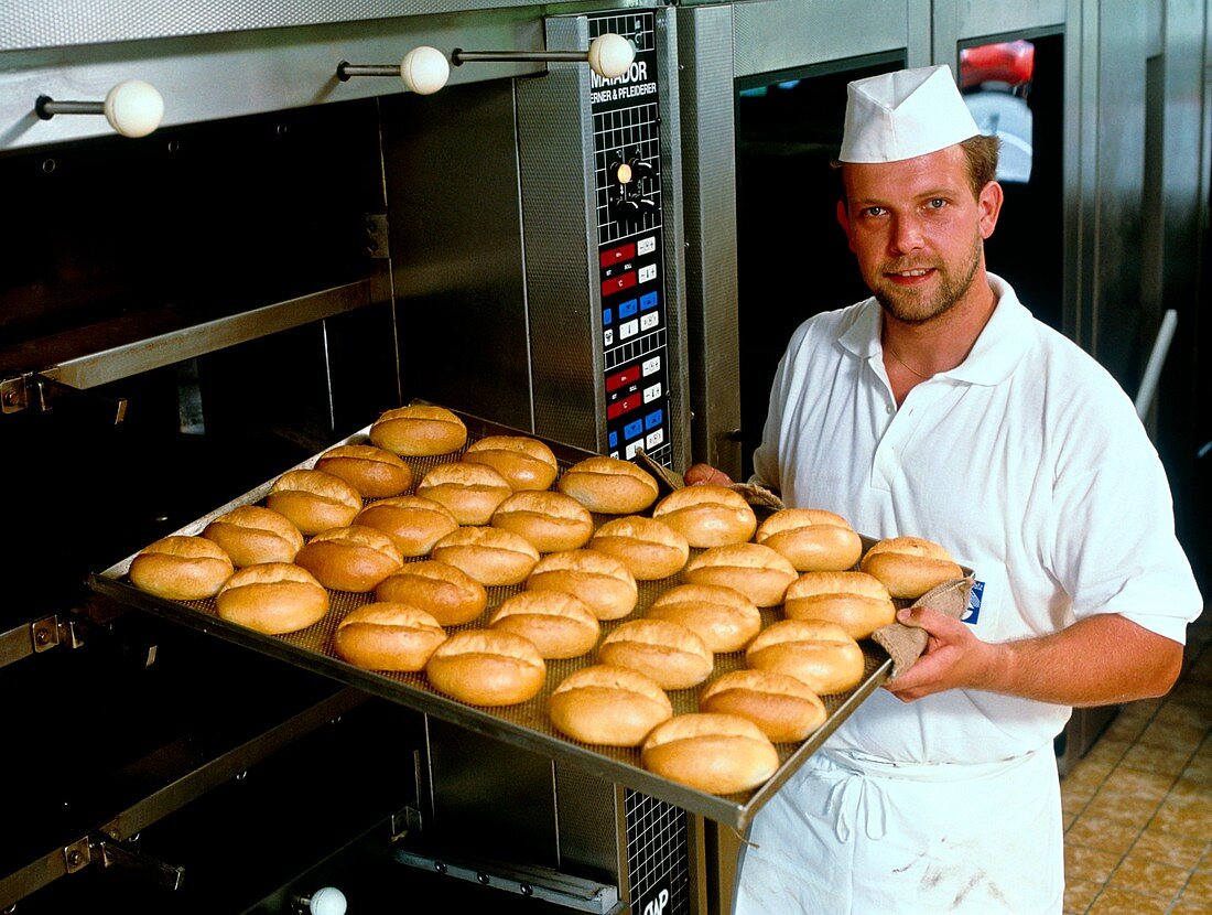 Man removing bread rolls from a bakery oven