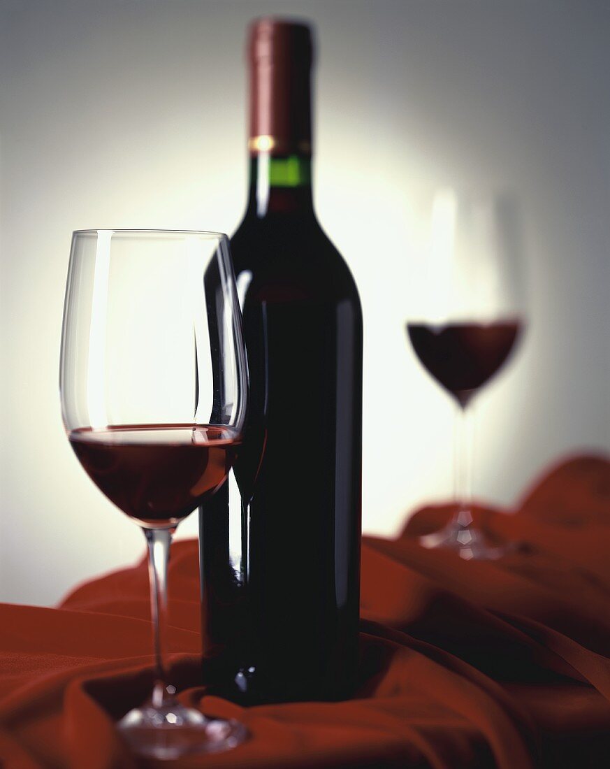 Rotweinstilleben mit zwei Gläsern und Flasche auf rotem Samt