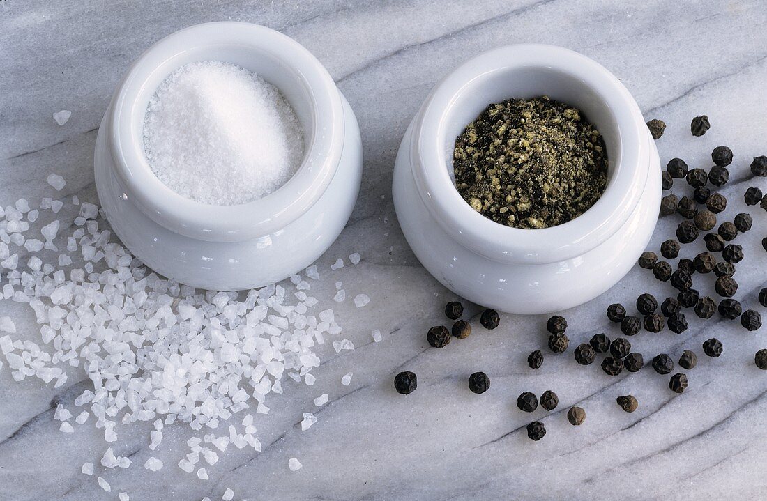 Salt and pepper in containers, peppercorns and sea salt