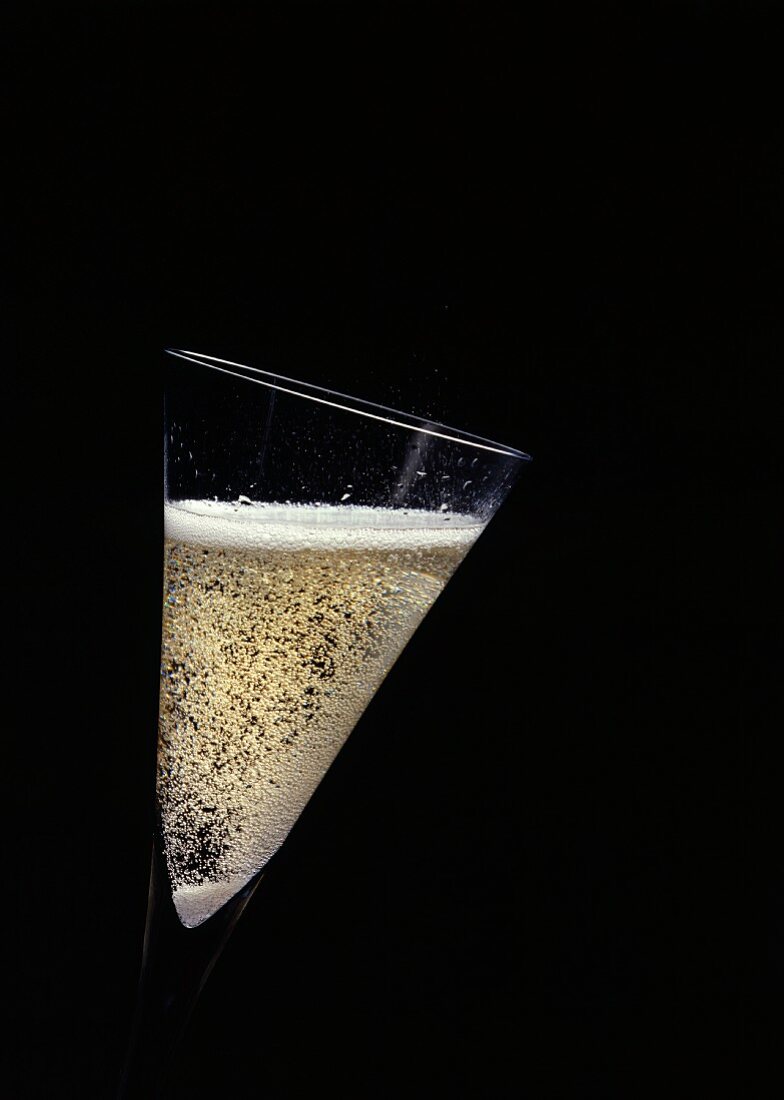 Ein schräg gehaltenes Glas mit perlendem Schaumwein
