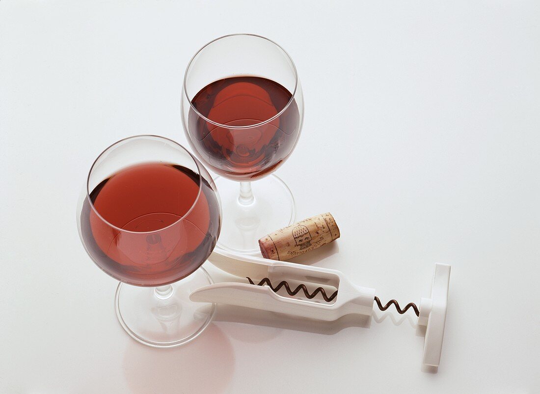 Two different red wine glasses, cork and corkscrew beside them