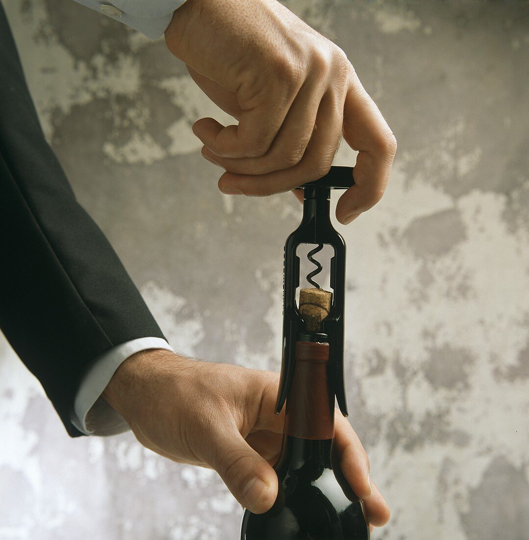 A Person Opening a Bottle of Red Wine with a Corkscrew