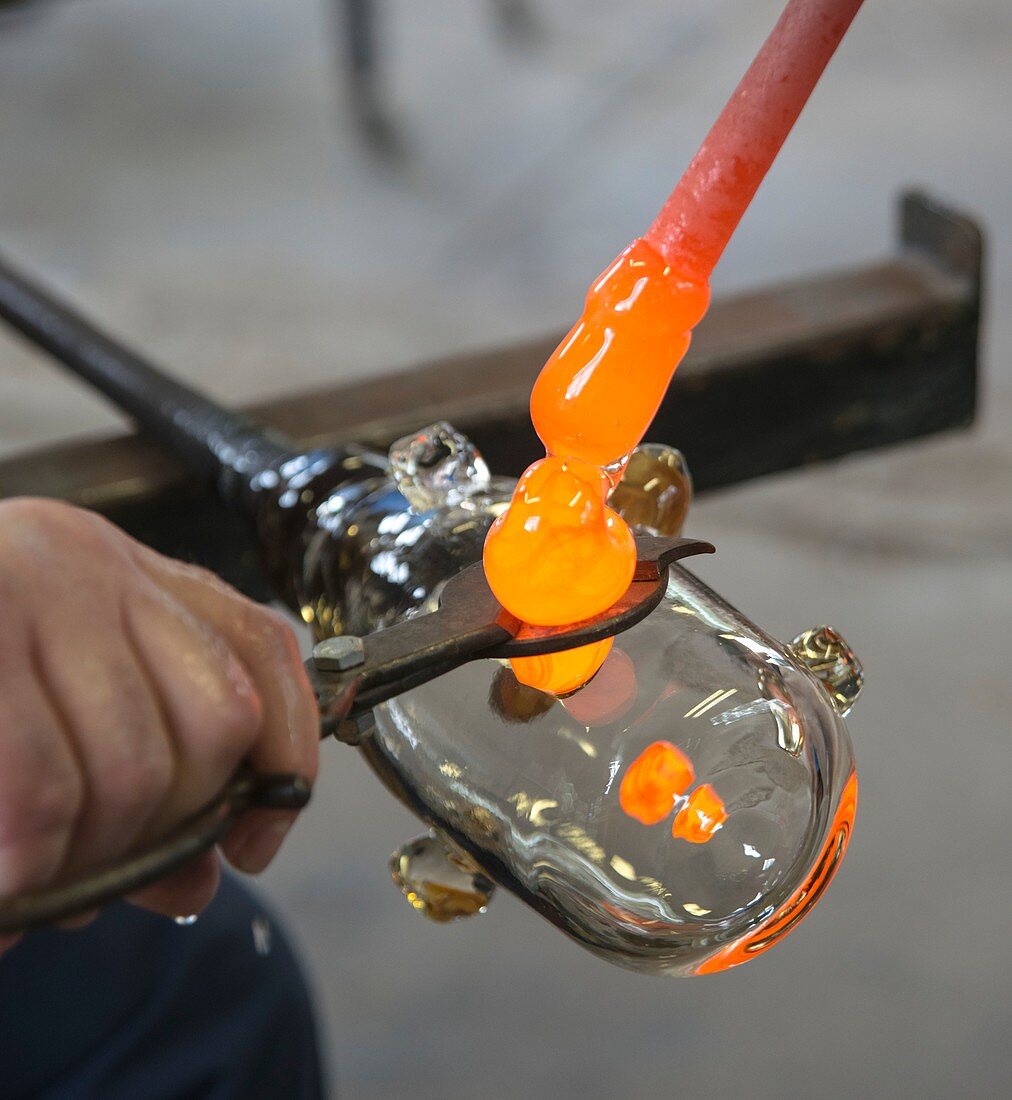 Glassblower cuts molten glass into shape