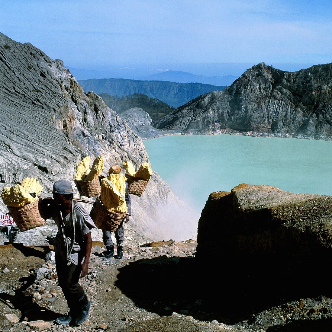 Men carrying mined sulphur from volcanic crater