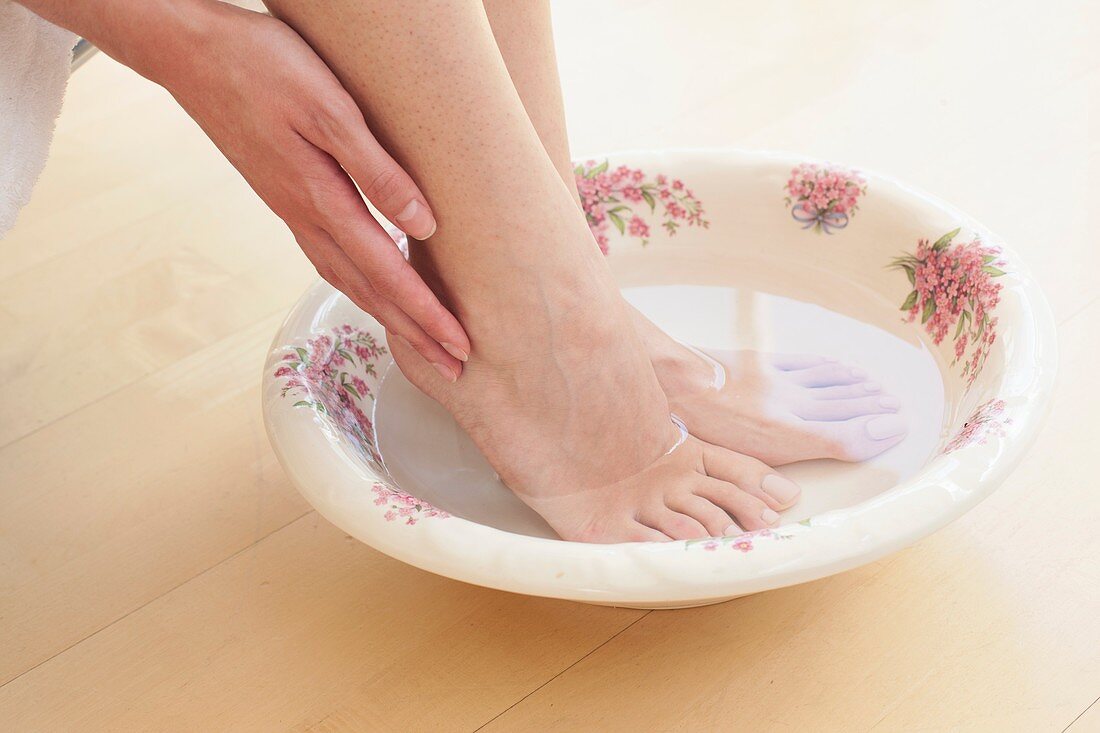 Young woman soaking feet in bowl of water