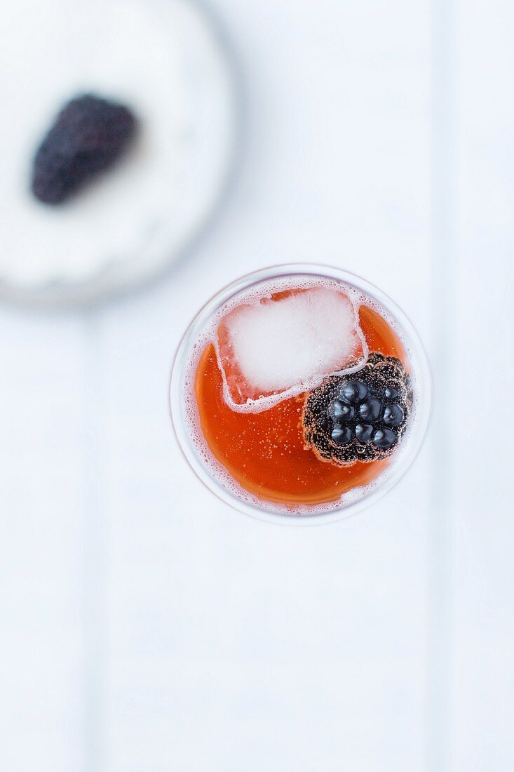 A kir cocktail with a blackberry and an ice cube