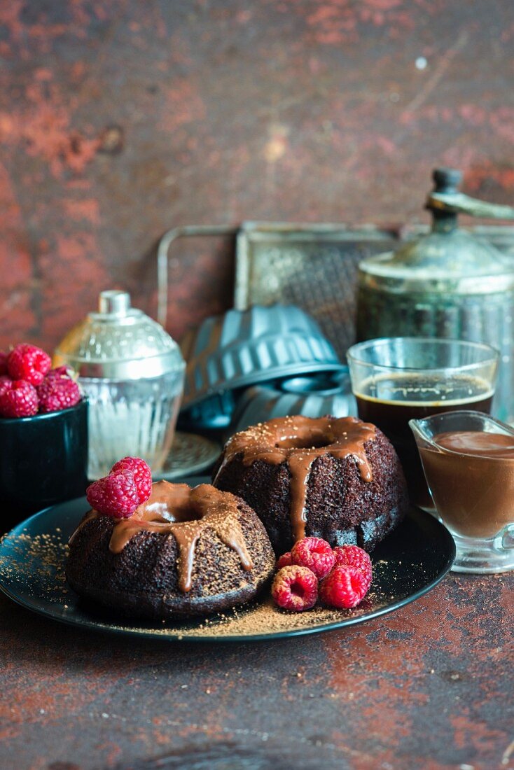 Kleine Schokoladennapfkuchen mit Schokoladen-Sauerrahm-Glasur und frischen Himbeeren
