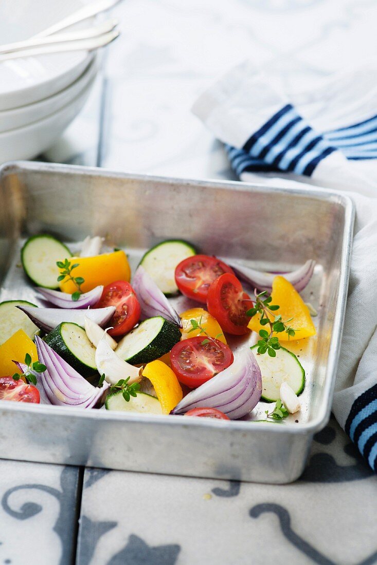 Fresh vegetables in a roasting tin (courgette, onion, tomatoes, yellow pepper, garlic and thyme)
