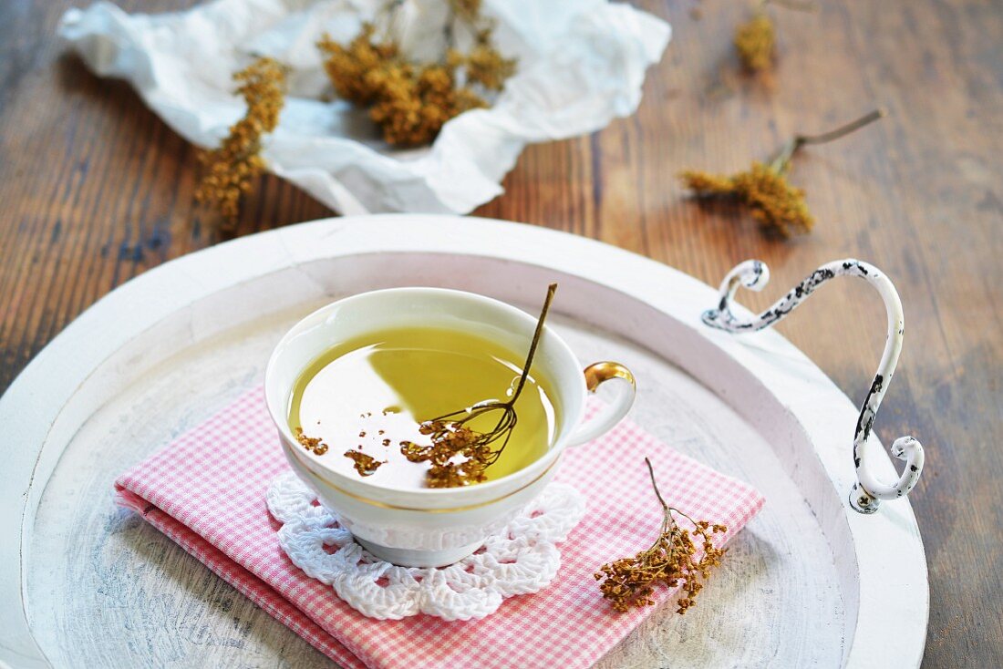 Elderflower tea in a teacup on a tray in front of dried elderflower