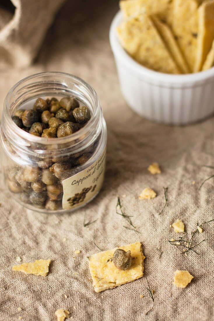 Capers in a glass jar next to crackers
