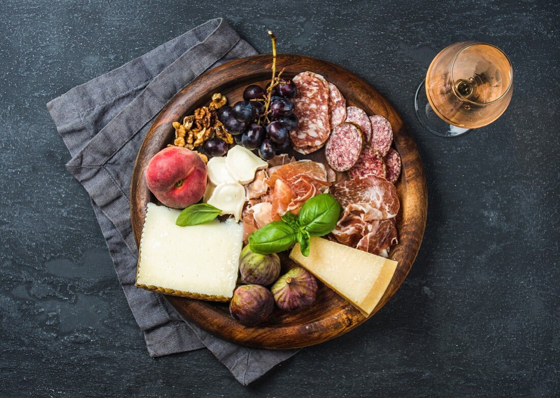 Parmaschinken, Salami, Käse, Feigen, Trauben, Pfirsich, Walnüsse und Basilikum auf Holzbrett