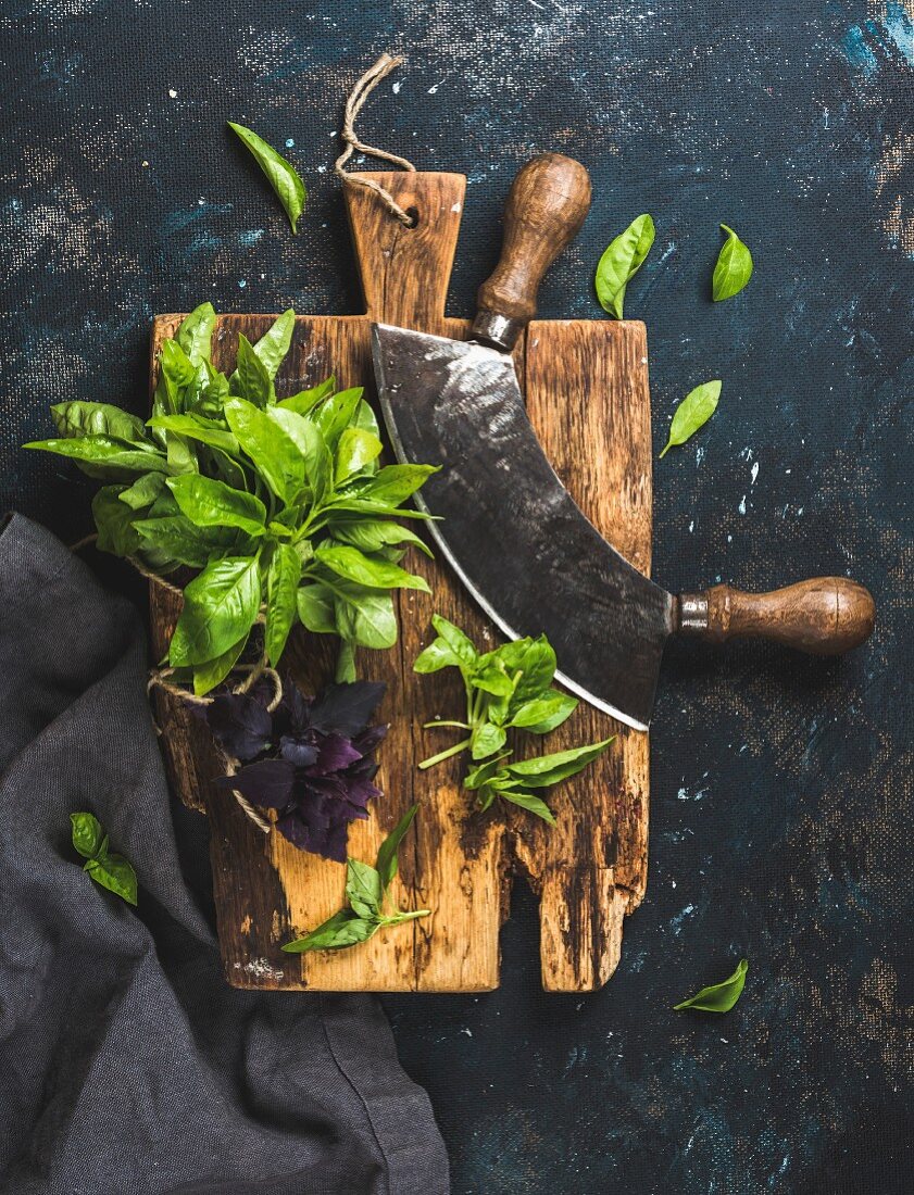Fresh green and purple basil leaves with herb chopper knife on rustic cutting board