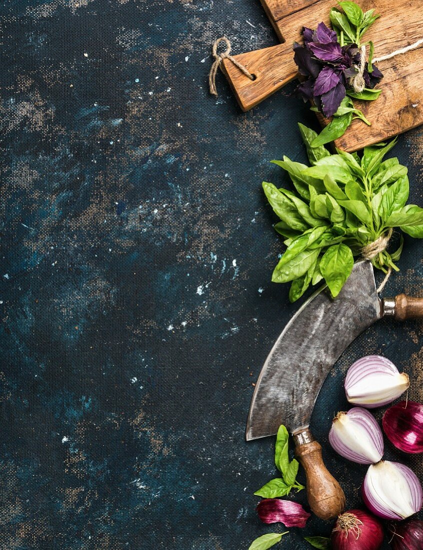 Green and purple basil, red onions and garlic with a mezzaluna and rustic chopping board